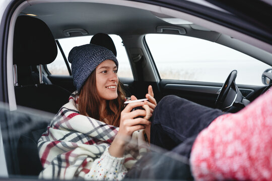 Handsome Girl Traveler Wearing Boho Scarf Rest In Car And Looking Away Winter Landscape. Young Woman Traveler Sitting At Car And Get Warm Cup Of Tea