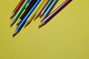 several multi-colored pencils lie on the yellow surface.