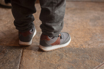 A closeup of a man wearing sneakers and gray pants, standing on the stone-tiled ground
