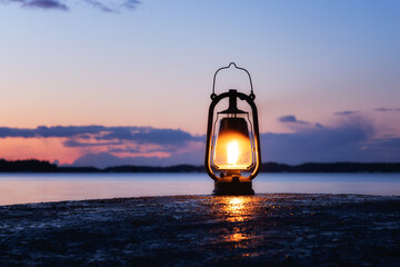 An old vintage oil lantern on a rock by the sea. Beautiful sunset sky and sea on background. Chill out travel concept.