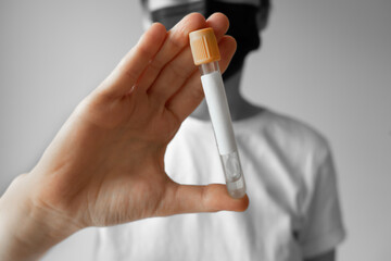 Young woman wearing a medical face mask holding a glass test tube in her hand. some areas are black and white, some areas colored. copy space for text. blank label.
