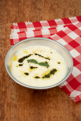 Traditional Turkish Yayla soup with yoghurt, rice and dried mint on wooden background and red and white checkered table cloth.	