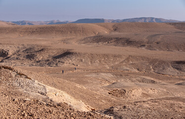 Male hiker on a hiking trail in a remote desert region. Panoramic landscape of colorful sandy hills and mountain folds.