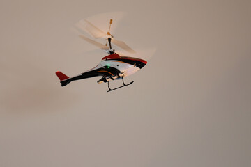 Radio-controlled indoor helicopter flying within a room and below a brass chandelier.