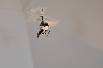 Radio-controlled indoor helicopter flying within a room and below a brass chandelier.
