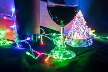wine glass and bottle and crystal christmas tree in shining bokeh garland on black background