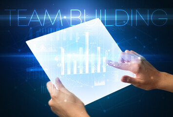 Hand holding futuristic tablet with TEAM BUILDING inscription above, modern business concept