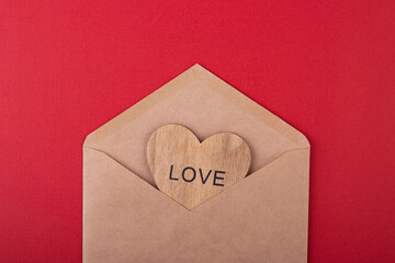 wooden heart with the inscription love in a craft envelope on a red background