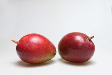 Two whole red mango fruits next to each other on a white background