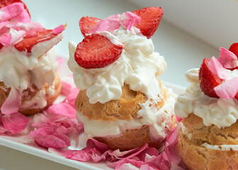 Delicious eclair with custard and whipped cream. French dessert with strawberries on a white porcelain dish. Decorated with rose petals. Healthy food.