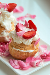 Delicious eclair with custard and whipped cream. French dessert with strawberries on a white porcelain dish. Decorated with rose petals. Healthy food.