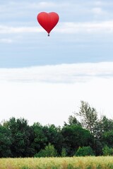 Red hot air balloon in shape of heart is landing on the green field