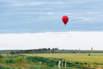 Fototapeta premium Red hot air balloon in shape of heart is landing on the green field