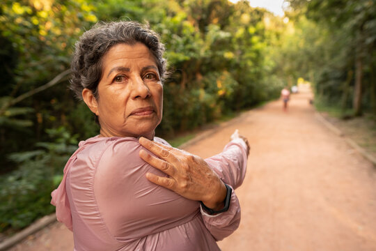 Senior mixed race woman looking at camera and stretching arms. Outdoor in green area. Overcome, healthy, fitness, freshness concept.