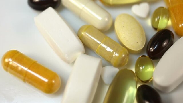 White, yellow, brown, transparent, black, oval and oblong tablets, pills and capsules, water and fat-soluble. Smooth motion in the frame, close-up, real time, on a white background, contains people