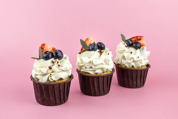 Delicious cupcakes with cream and fresh berries isolated on pink background. Copy space.