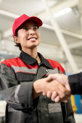 Young smiling female engineer in workwear looking at colleague during handshake