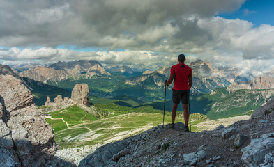 Fototapeta premium Person with trekking poles looking at mountains in Italian Dolomites