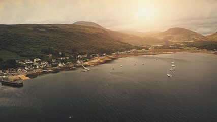 Sun over mountain aerial. Yachts, ships on ocean bay. Nobody nature seascape. Water transport at sea harbor. Summer vacation. Travel to Loch-Ranza Bay, Arran island, Scotland, United Kingdom, Europe