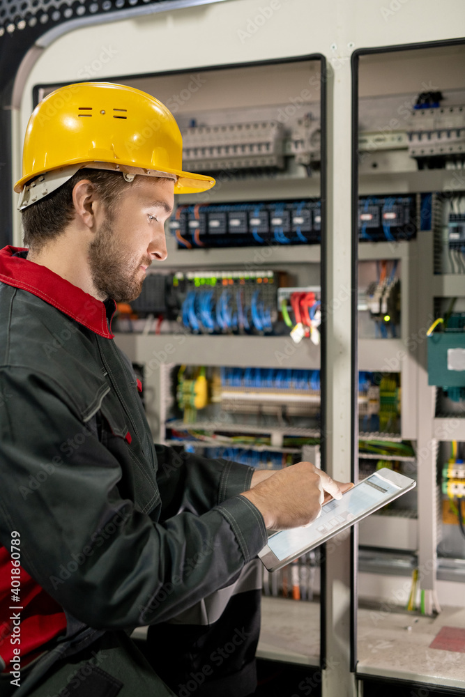 Poster young engineer in workwear and hardhat pointing at electronic sketch or scheme