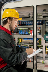 Young engineer in workwear and hardhat pointing at electronic sketch or scheme