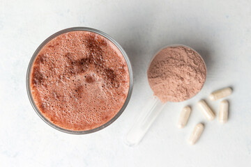 Glass with milkshake of whey protein isolate, protein powder in scoop, white capsules of amino...