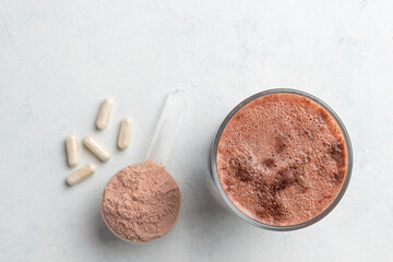 Glass with milkshake of whey protein isolate, protein powder in scoop, white capsules of amino acids and creatine, bodybuilding food supplements on white background, top view, flat lay
