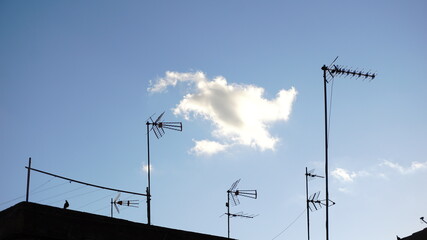 silhouettes of television antennas against cloud sky