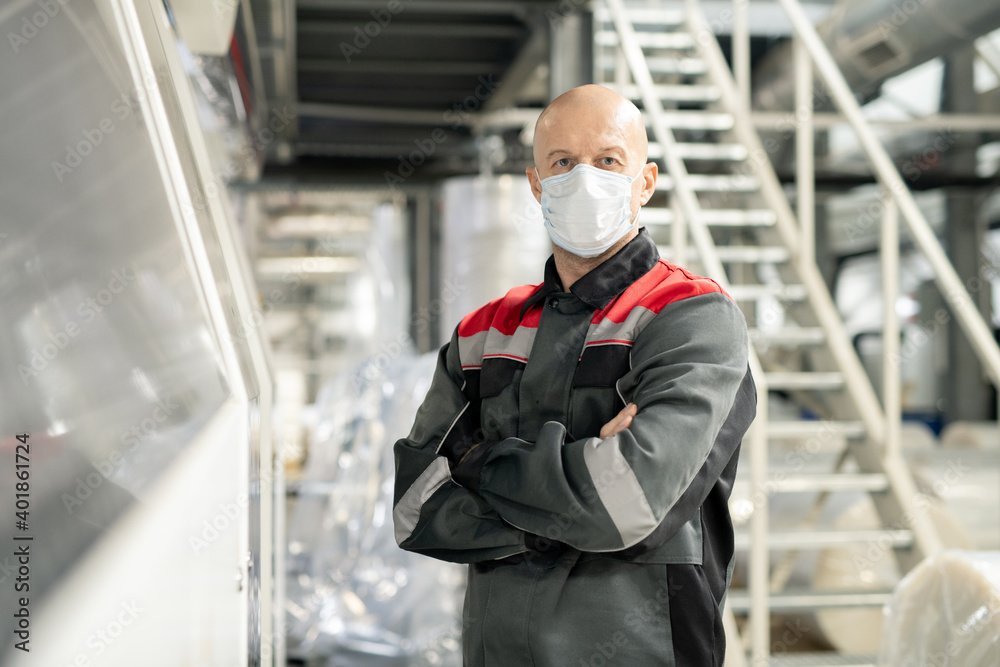 Poster bald mature worker of polymer processing factory in workwear and protective mask