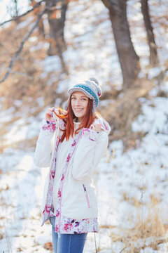Young fashionable girl smiling and posing in a white down jacket and a blue patterned warm hat during a walk in the winter woods