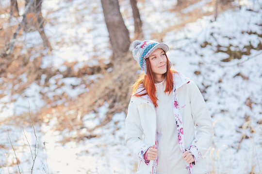 Young redheaded hiker walking through the winter woods in warm light clothing and smiling mischievously, looking out into the distance