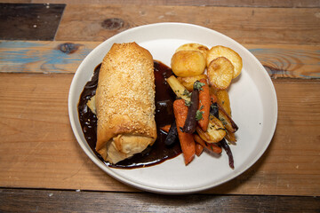 A delicious plate of Jackfruit, stage and Onion strudel on a wooden restaurant table
