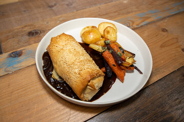 A delicious plate of Jackfruit, stage and Onion strudel on a wooden restaurant table