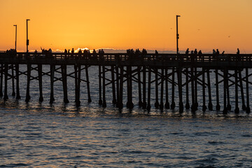 Evening walkers and fishermen line the pier at sunset off the coast of Southern California on a cold winter's day.