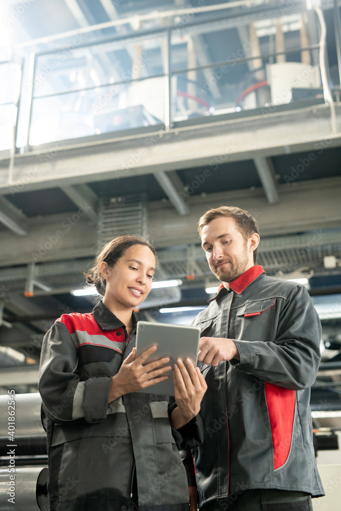 Poster young quality control managers of contemporary factory scrolling through data