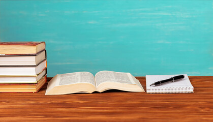 Open book on the table, notebook, pen on a blue background.