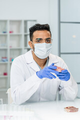 Young gloved male scientific researcher in whitecoat, mask and eyeglasses