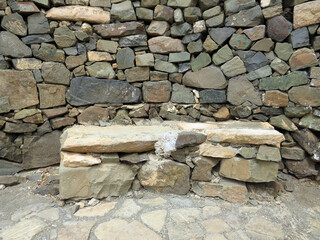 Stone bench in a wall of rocks of different sizes and shapes. Ancient archeology and construction background.