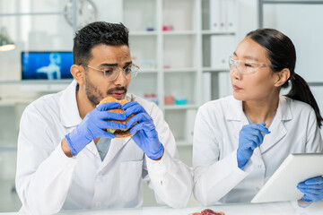 Worker of food control eating hamburger and describing its taste to colleague