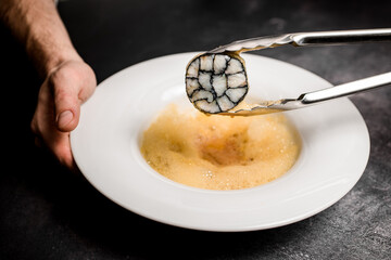 Close-up of male hand holding plate of molecular froth and tongs with fish roll slice