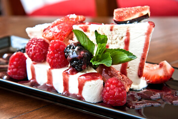 Frozen meringue dessert with red berry sauce and figs served, on a black plate on wooden background