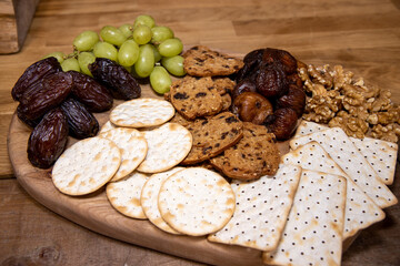 A wooden tray selection of winter cheese biscuits, nuts and grapes