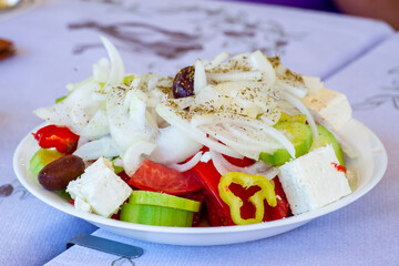 Traditional fresh Greek salad on a plate on a table with tablecloth in taverna, Greece. National cuisine experience