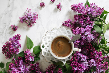 Obraz na płótnie Canvas A cup of coffee surrounded by lilacs on a marble table