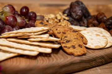 A wooden tray selection of winter cheese biscuits, nuts and grapes