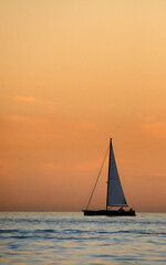 Fototapeta na wymiar vertical image of orange sky at sunset and silhouette of sailboat in corona del mar beach orange county California