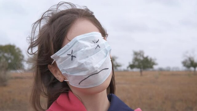 Face in a protective mask. Girl with a protective mask with a painted killed emoticon. Coronavirus kills concept.