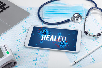 Tablet pc and doctor tools on white surface with HEALED inscription, pandemic concept