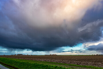 Wintry shower with fall streaks of rain and small hail over flat dutch countryside