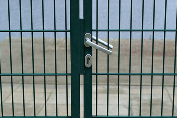 closeup of metallic lock on closed door of the green metal fence with blurred concrete beach and the lake in the background